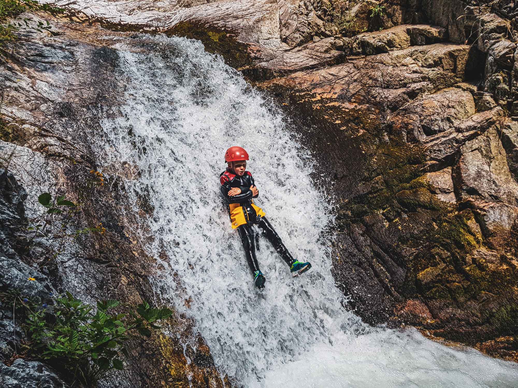 Un jeune enfant glissant dans un toboggan naturel sur le parcours canyoning Azéro avec Nature Canyon Ardèche
