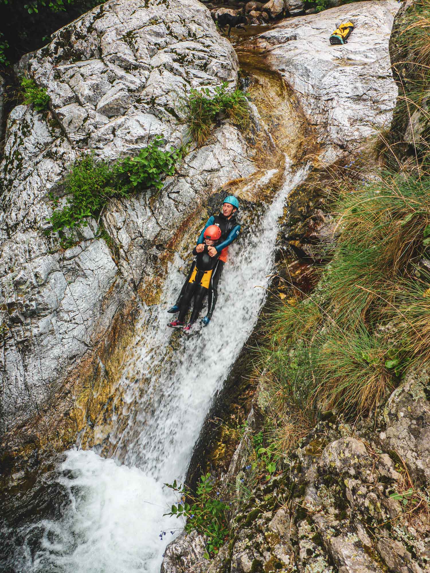 Un père et son fils se laissant glisser sur un toboggan naturel sur le parcours canyoning de l'Azéro avec Nature Canyon Ardèche
